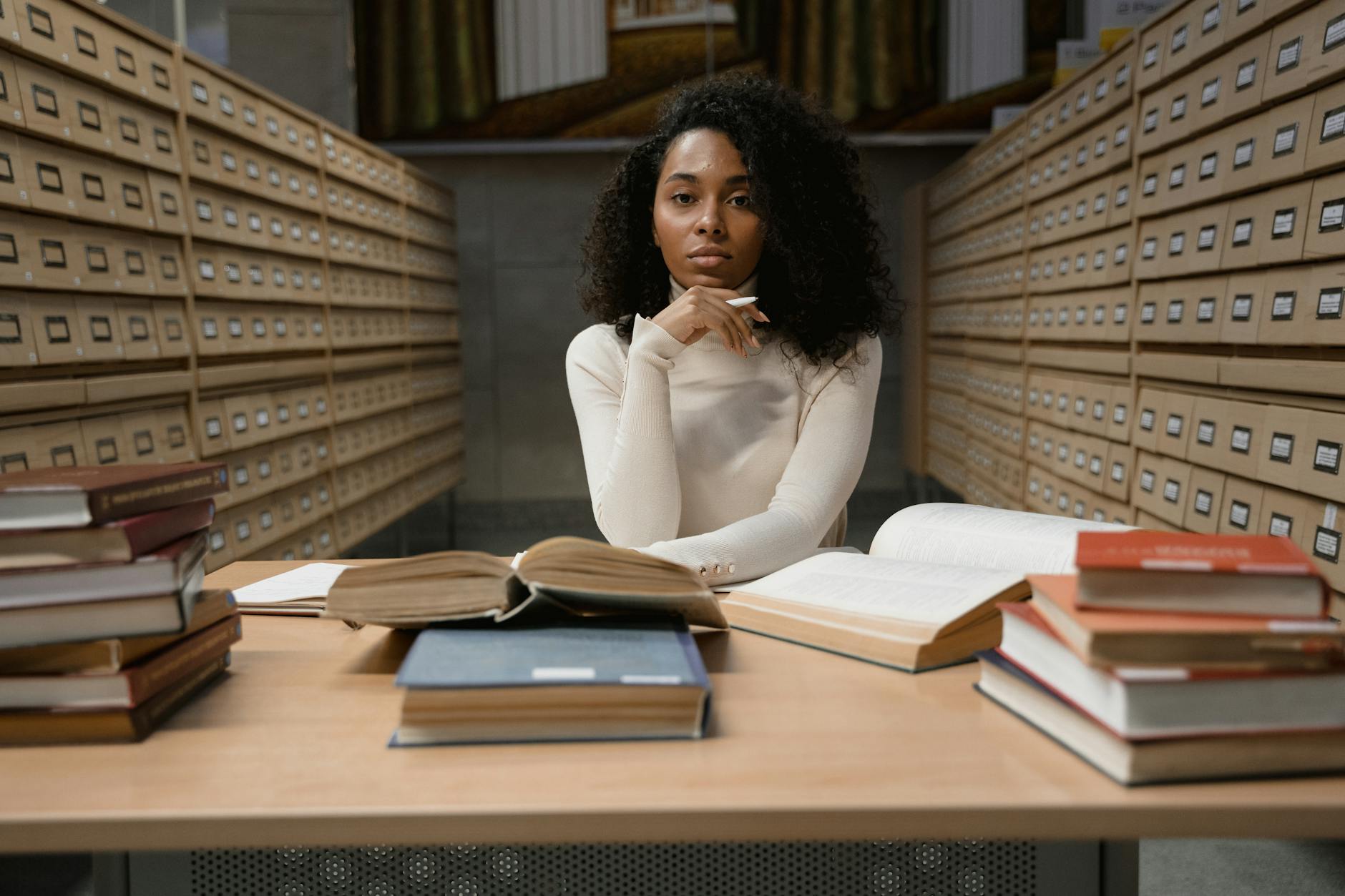 a woman with curly hair sitting on a table with stacks of books
